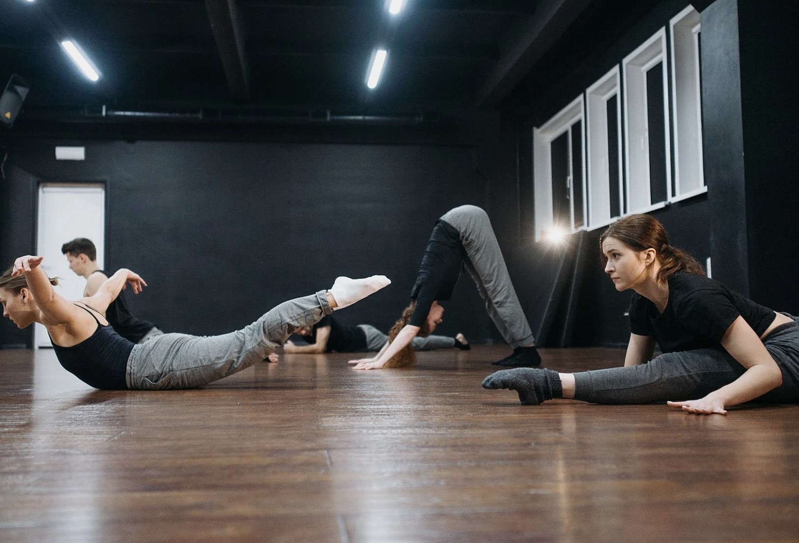 木製の床の上で室内にて、大人のグループがダンスの柔軟体操を一緒に練習している。